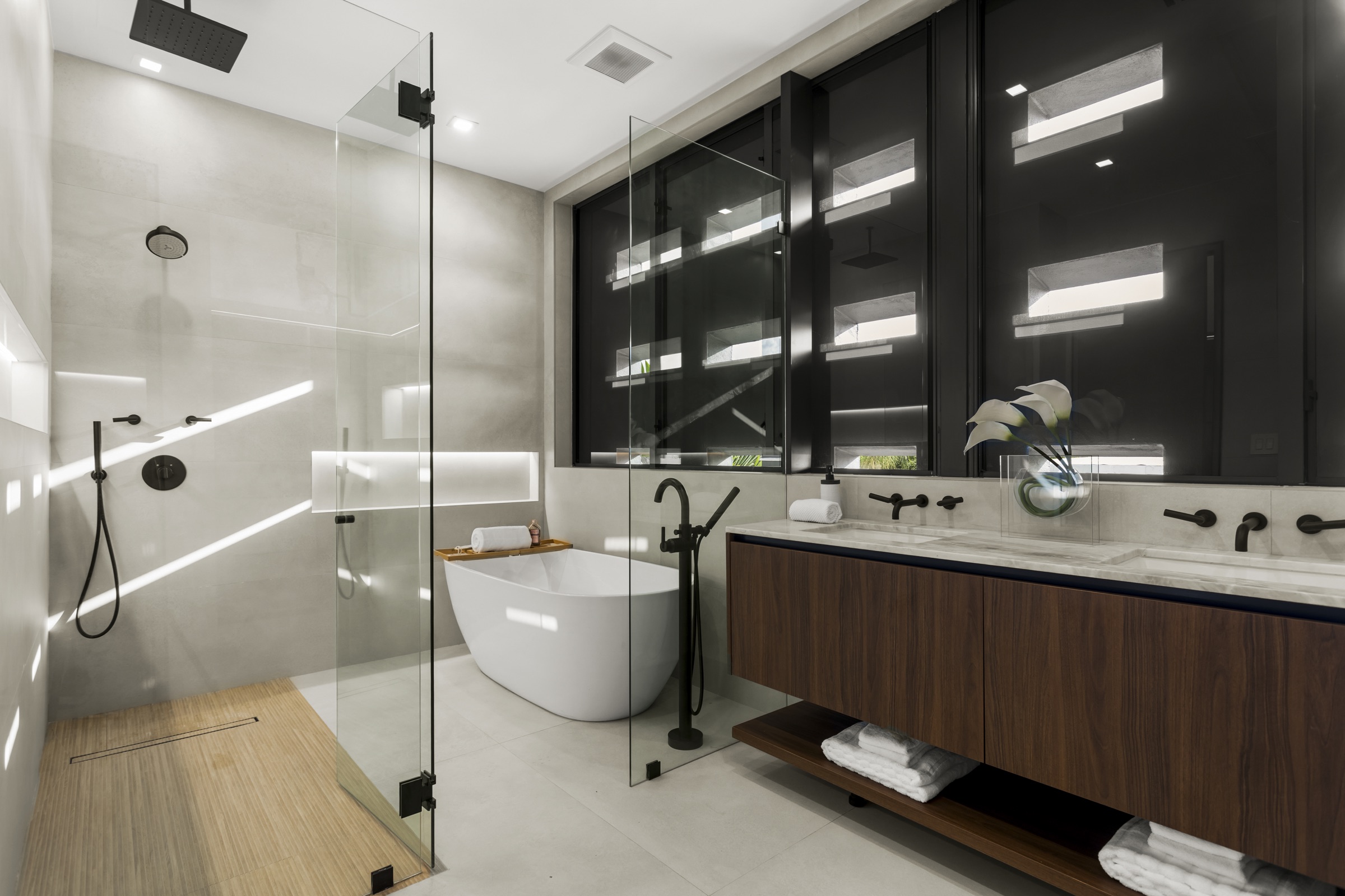 Baño principal con mueble de madera, superficies de piedra y luz horizontal filtrada en Fair Isle Residence