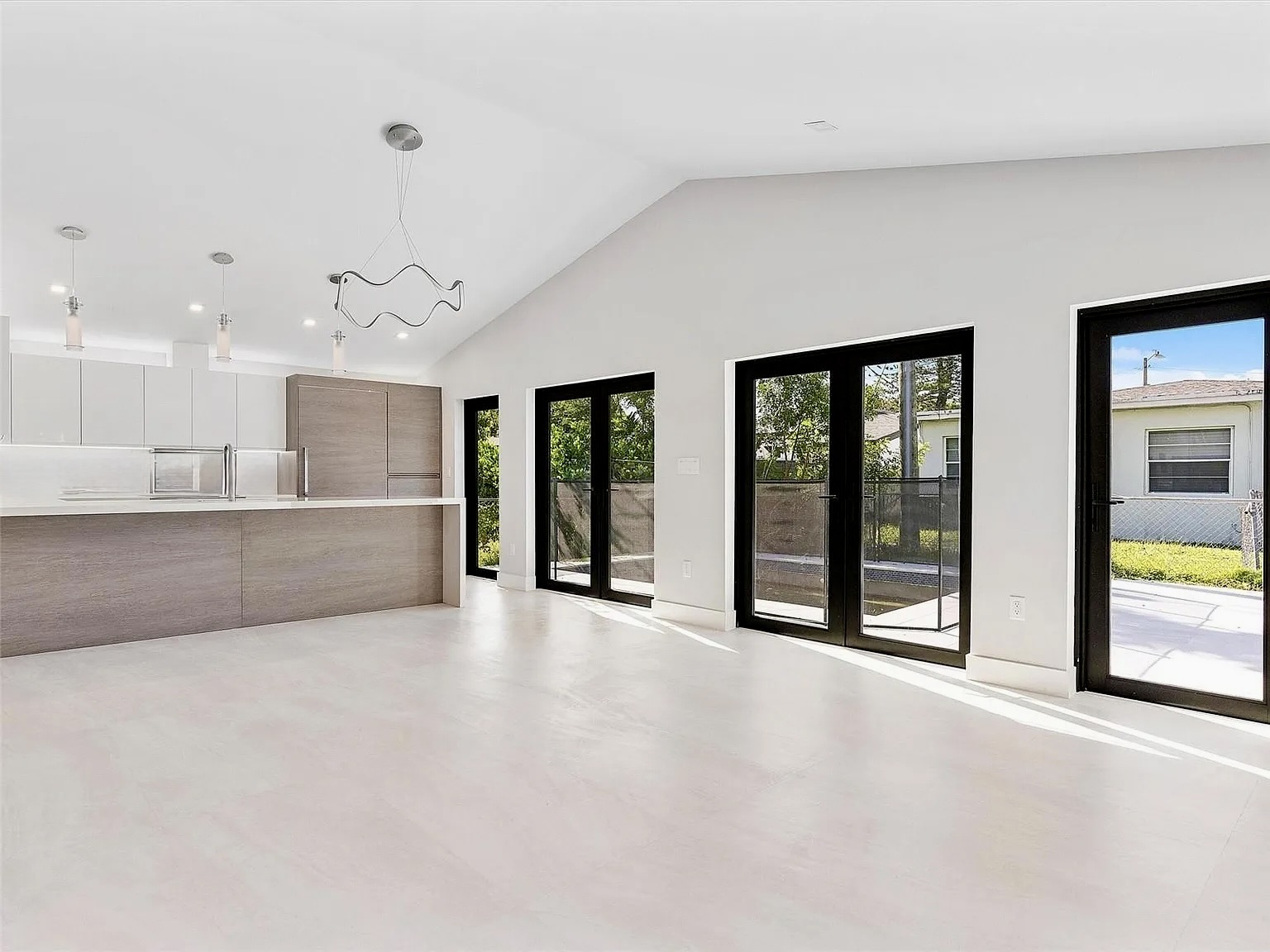 Cocina y sala abiertas terminadas en Frow Avenue Residence con techo elevado y puertas de marco oscuro