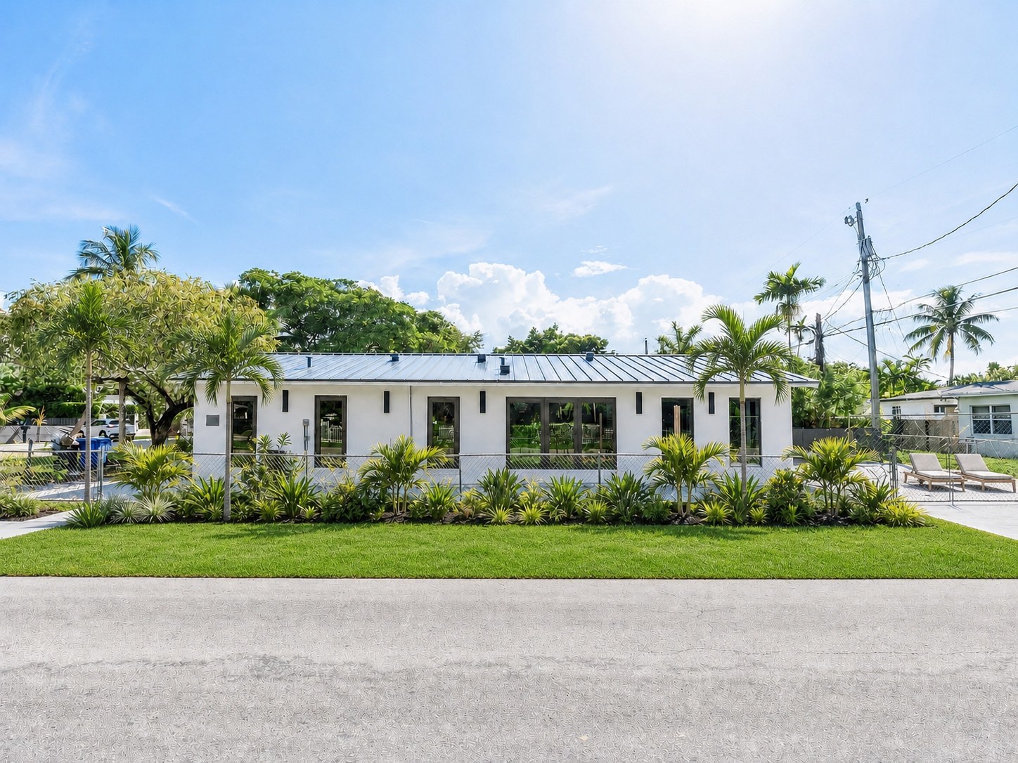 Fachada ajardinada de Frow Avenue Residence con exterior blanco, cubierta metálica, palmeras y aperturas oscuras