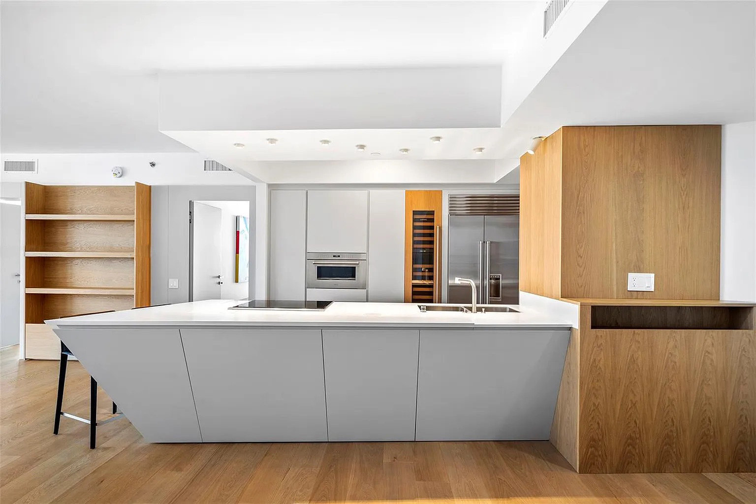 Isla de cocina a medida con frentes grises, encimera blanca y madera cálida en Icon South Beach Apartment