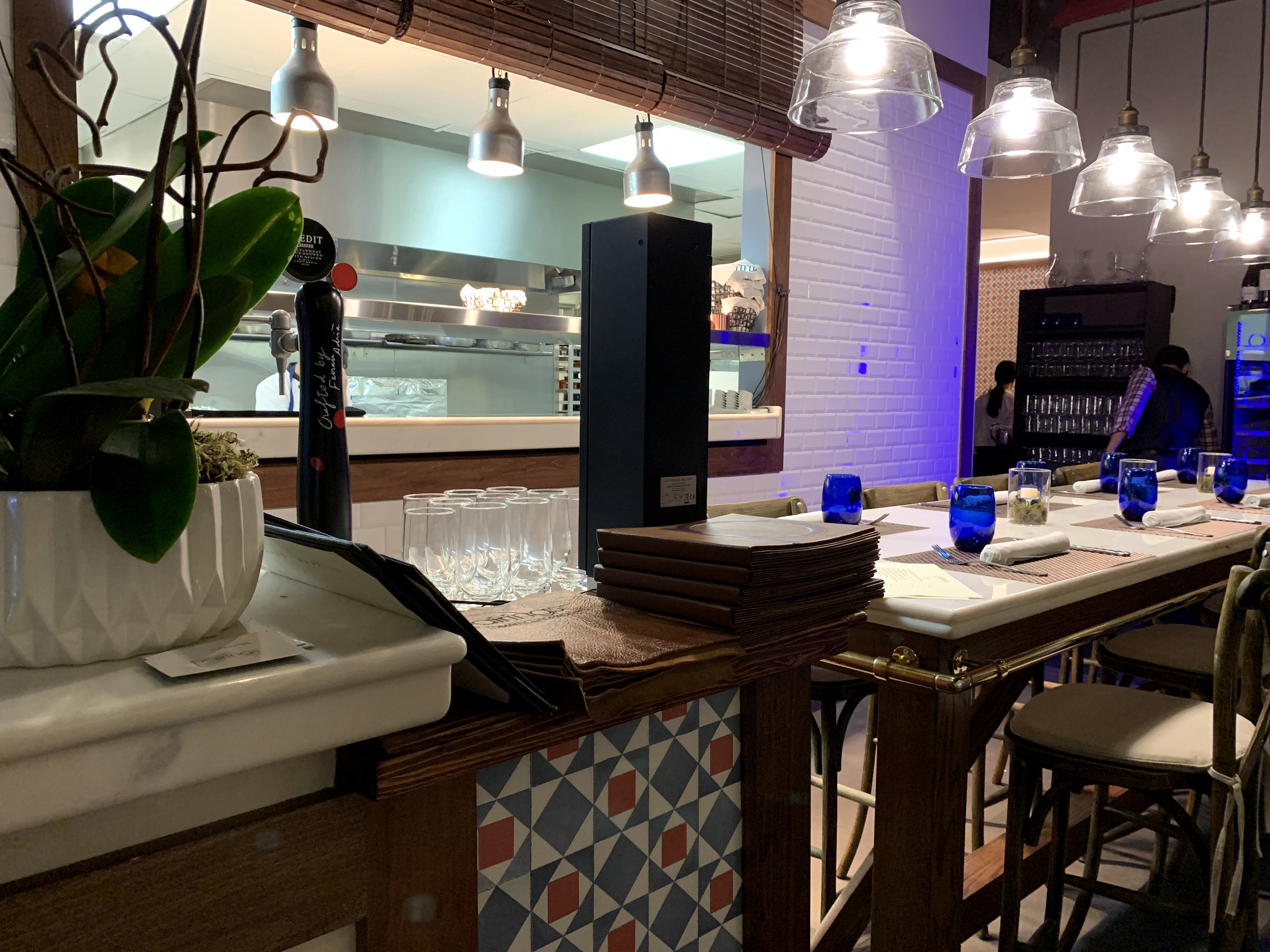 Mostrador de Pairings Restaurant con cerámica geométrica, madera, flores y cocina abierta al fondo