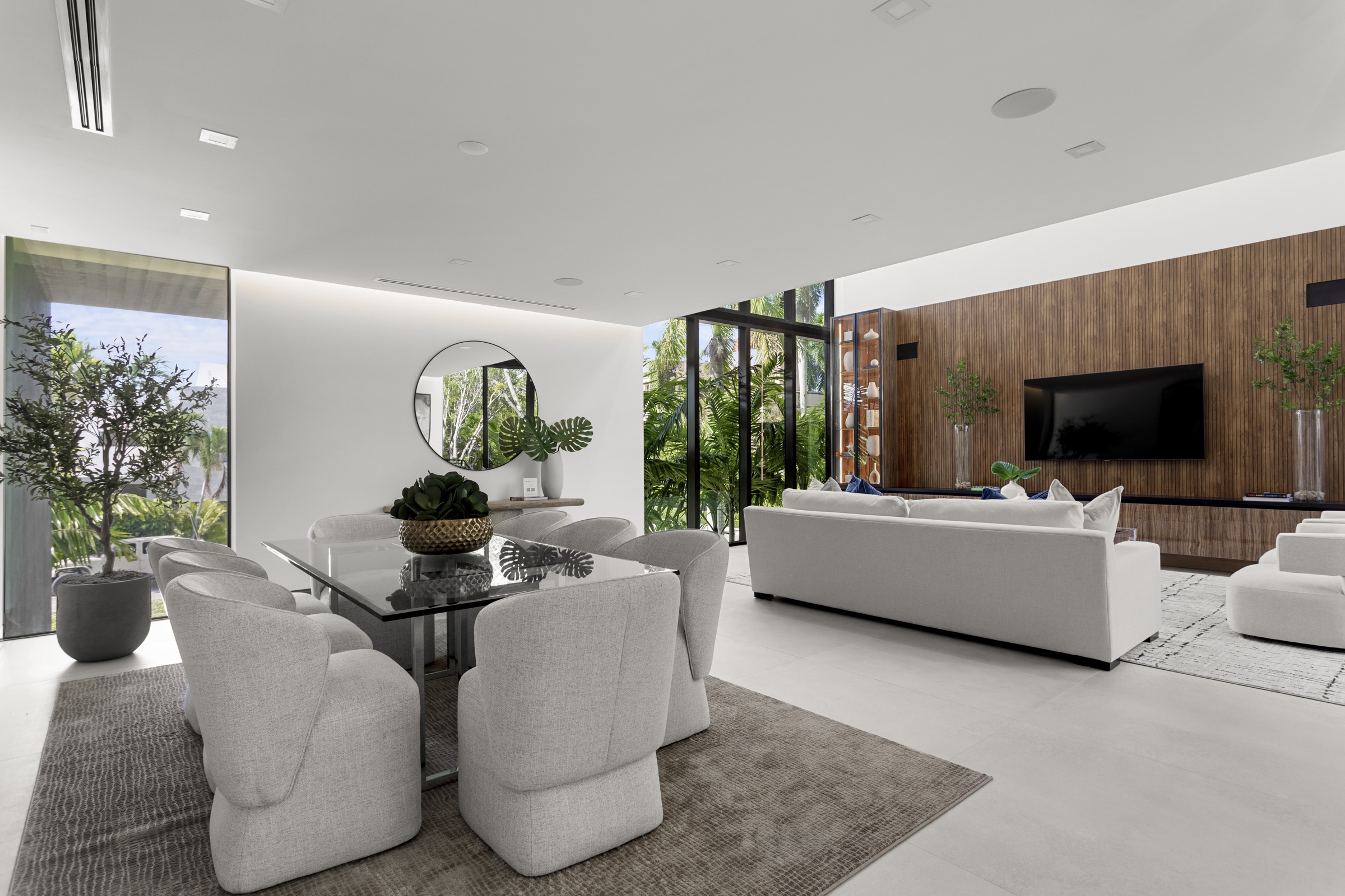 Open living and dining room with warm wood wall and tropical views at Fair Isle Residence