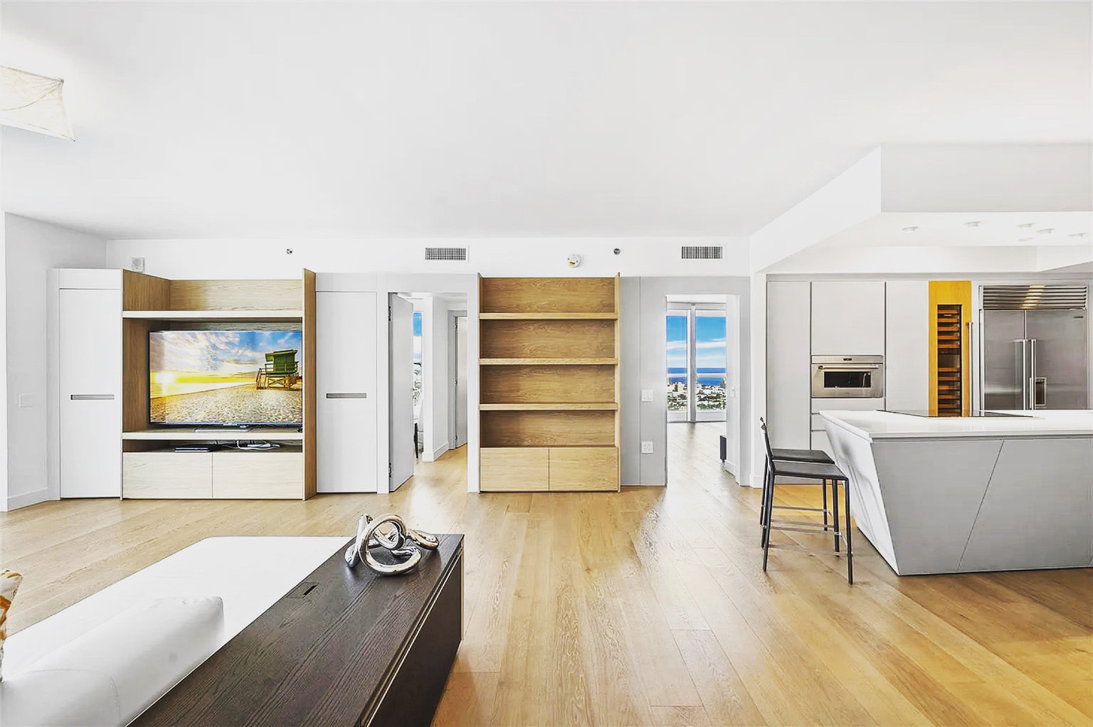 Continuous living and kitchen space at Icon South Beach Apartment with integrated cabinetry and warm oak flooring