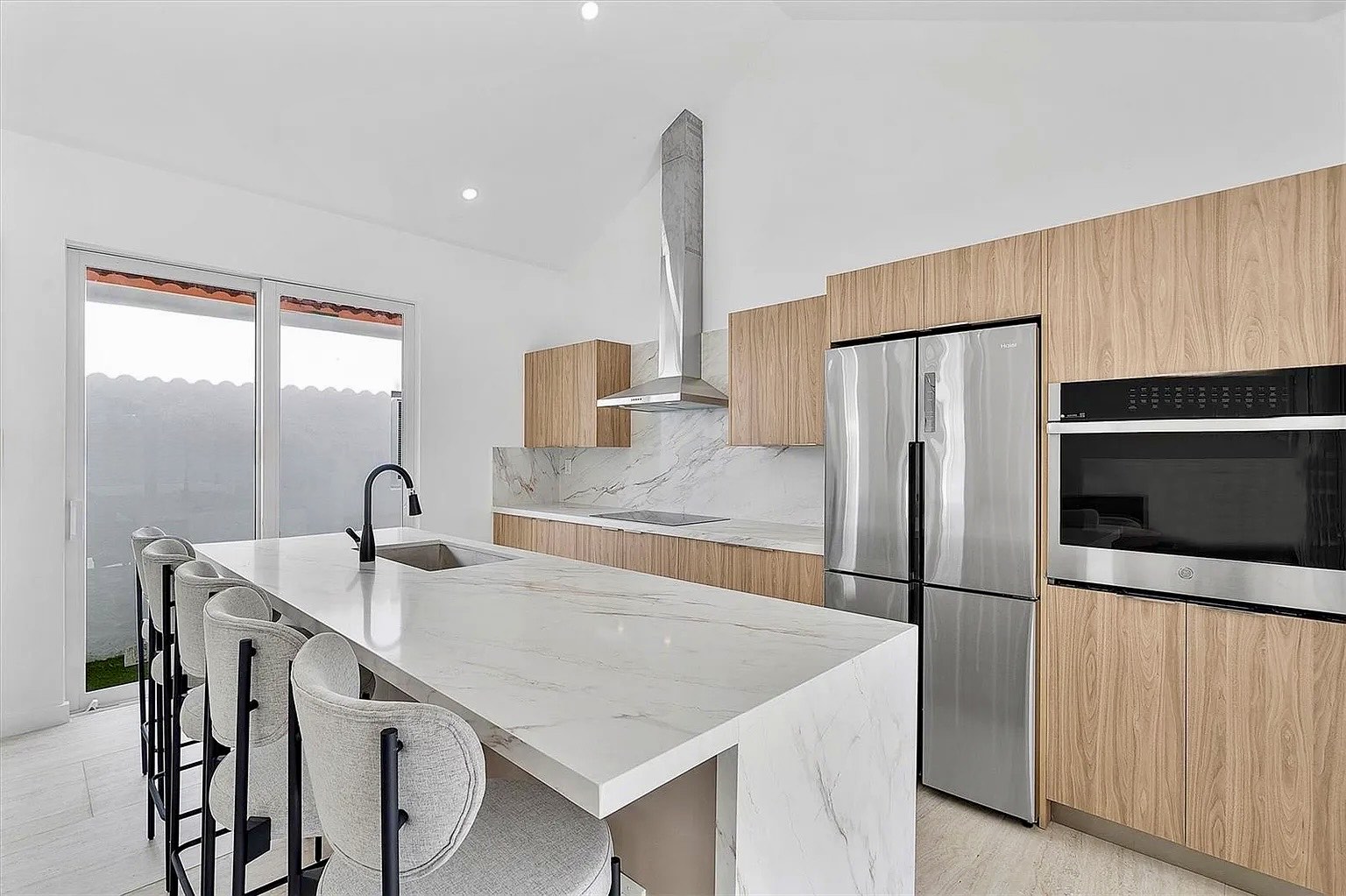 Open kitchen at NE 45th Street Residence with warm timber cabinetry, pale stone surfaces and a large island